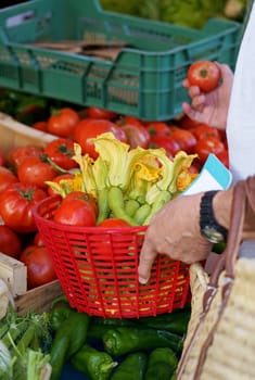 Close-up of a man shopping, collecting fresh tomatoes and zucchini in a grocery cart at a local market, store or supermarket.