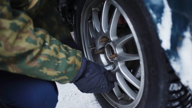 Close-up of spinning wheels in winter. Clip. Man spins wheels on highway in winter. Man changed the wheel and tighten screws.