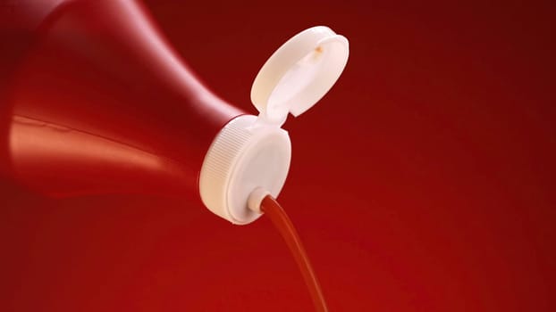 Ketchup, tomato sauce isolated on red background. Close up of ketchup pouring out of plastic bottle with white lid, concept of food preparation.