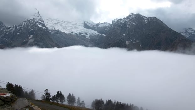 Fly over majestic mountain peaks and a fog. Creative. Valley covered by clouds and mountains on the background