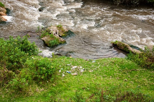rio contaminado de color marron con maderas de residuos entre las rocas y mucha basura con plasticos en la orilla del mismo rio. High quality photo