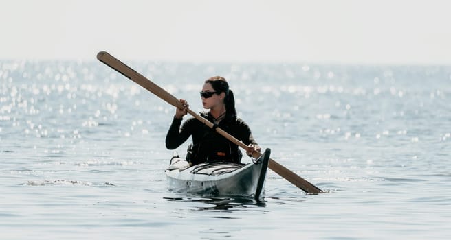 Happy smiling woman in kayak on ocean, paddling with wooden oar. Calm sea water and horizon in background