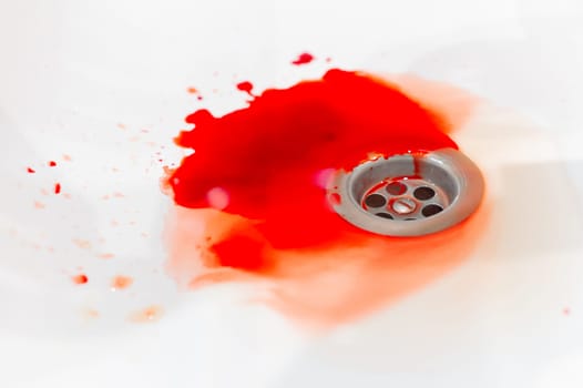 Blood flows over a white bathroom sink. Blood stains in the drain hole. Sink with streams of blood. Red paint drips down the sink drain. Accident with human injuries. Bleeding in the bathroom.