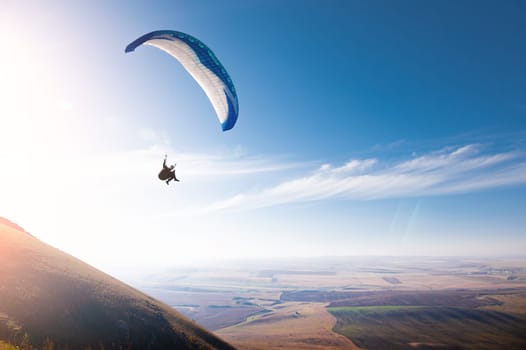 A paraglider flies in the blue sky against a background of clouds and blue sky. Paragliding in the sky on a sunny day