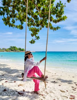 Asian woman on a swing at the beach of Koh Samet Island Rayong Thailand, the white tropical beach of Samed Island with a turqouse colored ocean on a sunny afternoon