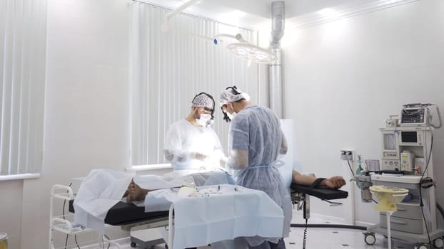 Team of doctors perform surgery while patient is under anesthesia. View inside of the operating room with men surgeons and sedated male patient.