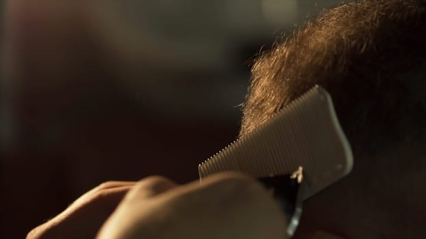Man gets a cool haircut in barbershop. Frame. Hands of professional hair stylist cutting client shot hair. Close up of beautician's hand with scissors. Selective focus. Barber makes the cut man electric razor. Men's care head. Soft focus