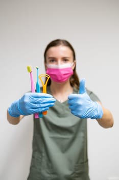 Dentist holding toothbrushes and shows thumb up, vertical photo.