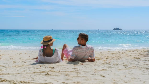 A couple of men and woman sitting on the beach looking out over the ocean of Koh Samet Island Rayong Thailand, the white tropical beach of Samed Island with a turqouse colored ocean