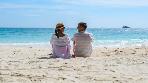 A couple of men and woman sitting on the beach looking out over the ocean of Koh Samet Island Rayong Thailand, the white tropical beach of Samed Island with a turqouse colored ocean