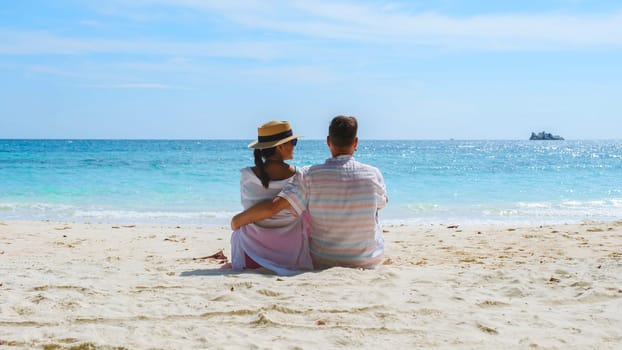 A couple of men and woman sitting on the beach looking out over the ocean of Koh Samet Island Rayong Thailand, the white tropical beach of Samed Island with a turqouse colored ocean on a sunny day