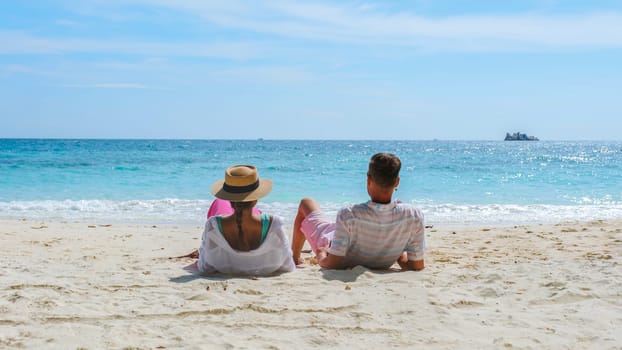 A couple of men and woman sitting on the beach looking out over the ocean of Koh Samet Island Rayong Thailand, the white tropical beach of Samed Island with a turqouse colored ocean on a sunny day