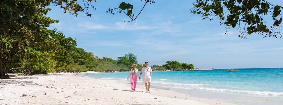 A couple of men and woman walking on the beach of Koh Samet Island Rayong Thailand, the white tropical beach of Samed Island with a turqouse colored ocean