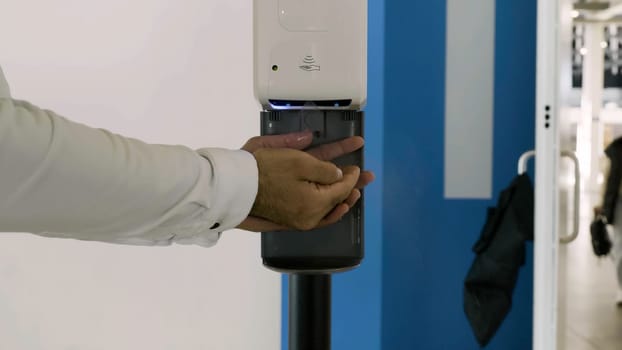 Close up of male hands using automatic alcohol gel dispenser. HDR. Spraying antiseptic on hands, prevention against COVID-19, new normal under Coronavirus