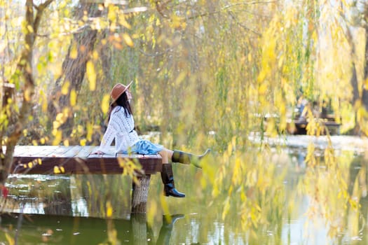 Autumn lake woman. She sits by a pond on a wooden pier in autumn and admires nature. The concept of tourism, weekends outside the city