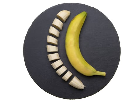one sliced and one whole banana on a black stone plate isolated on a transparent background
