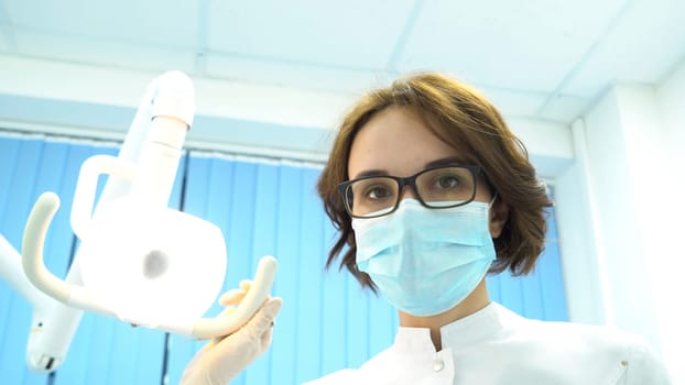 First person view of a young female dentist in mask approaches with Tools. Young doctor standing over the patient, looking at camera.