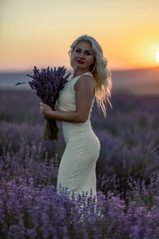 Blonde woman poses in lavender field at sunset. Happy woman in white dress holds lavender bouquet. Aromatherapy concept, lavender oil, photo session in lavender.