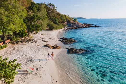Koh Samet Island Thailand, aerial drone view at a couple of men and woman on the beach of Samed Island in Thailand with a turqouse colored ocean and a white tropical beach in the morning sun