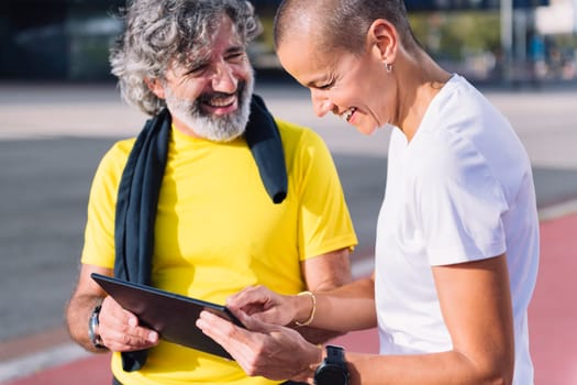 senior sports man laughing happy with personal trainer while planning workout on a tablet, concept of healthy and active lifestyle in middle age