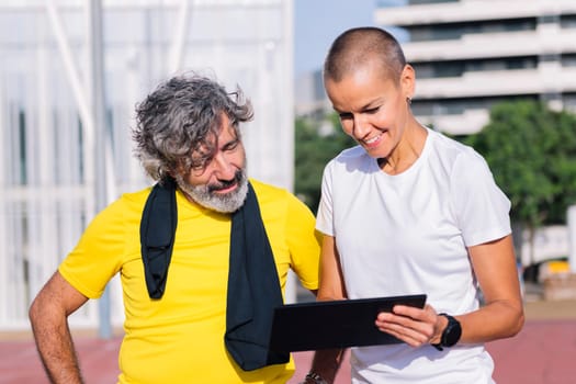 smiling female personal trainer planning workout with a tablet for a senior sports man, concept of healthy and active lifestyle in middle age