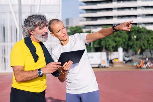 elderly sports man planning workout on a tablet with female personal trainer, concept of healthy and active lifestyle in middle age