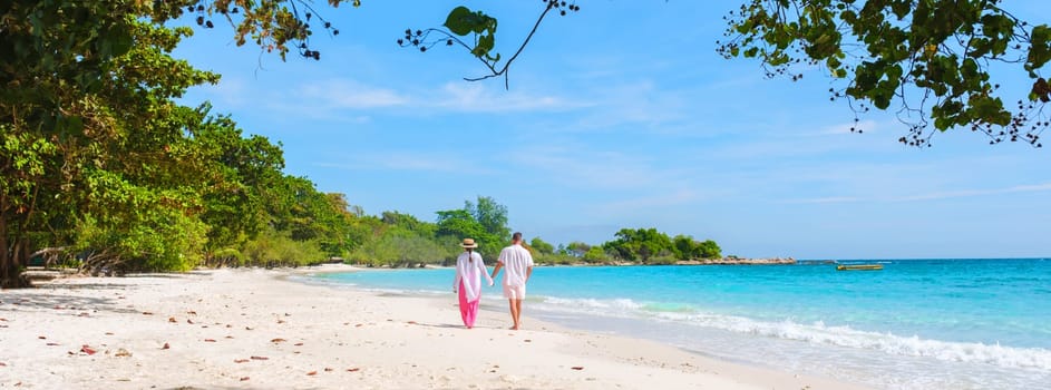 A couple of men and woman walking on the beach of Koh Samet Island Thailand, the white tropical beach of Samed Island with a turqouse colored ocean, Asian Thai woman and European men on the beach