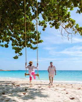 A couple of men and women at a swing on the beach of Koh Samet Island Rayong Thailand, the white tropical beach of Samed Island with a turqouse colored ocean.