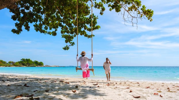 A couple of men and women at a swing on the beach of Koh Samet Island Rayong Thailand, the white tropical beach of Samed Island with a turqouse colored ocean.