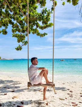 Men sitting on a swing at the beach of Koh Samet Island Rayong Thailand, the white tropical beach of Samed Island with a turqouse colored ocean