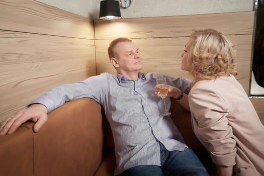 Loving adult couple communicates and embraces privately in the living room or in hotel. Woman is wearing business formal suit and man is wearing jeans and a shirt, indicating a close relationship