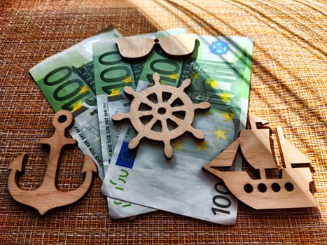 Euro paper money and wooden figurines with ship, a lighthouse, and a steering wheel. The concept of travel and its cost. The expensive price of a trip to the sea. Sailing