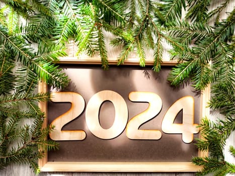 Wooden figures and numbers of the new year 2024 with frame and fir branches of Christmas tree. Celebration. Abstract background, pattern, frame, place for text, copy space