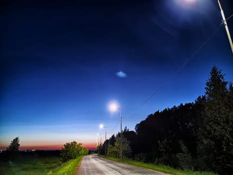 Asphalt road at night with lanterns on the side of road and the natural landscape around