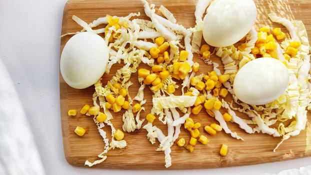 Chopped Peking cabbage, peeled eggs and yellow canned corn on cutting board as background. Cooking a healthy eco-friendly salad from natural products. Copy space and place for text