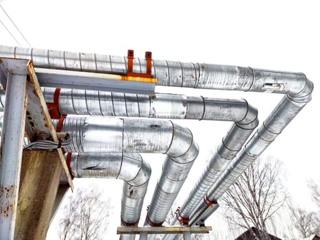 Metal pipes in thermal insulation winding outdoors and the over-illuminated white sky on background