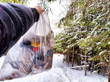 Bag of garbage in hand of woman and snow in forest on the background. A girl cleans up the trash after picnic. A tourist is going to throw garbage in nature. The concept of environmental pollution