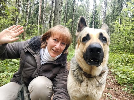 Adult girl with shepherd dog taking selfies in forest. Middle aged woman and big shepherd dog on nature. Friendship, love, communication, fun, hugs