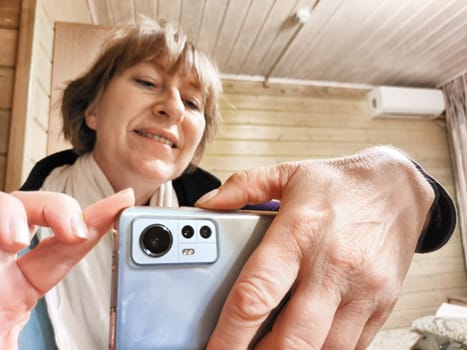 Middle-aged woman using smartphone for selfie and blogging. Female blogger poses in a photo. The girl admires herself in the mirror