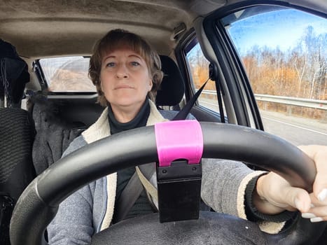 Portrait of female driver in solo journey. Adult mature woman holding steering wheel and looking through windscreen in travel by vehicle on vacation. Lady girl who is owner or rent car for travel