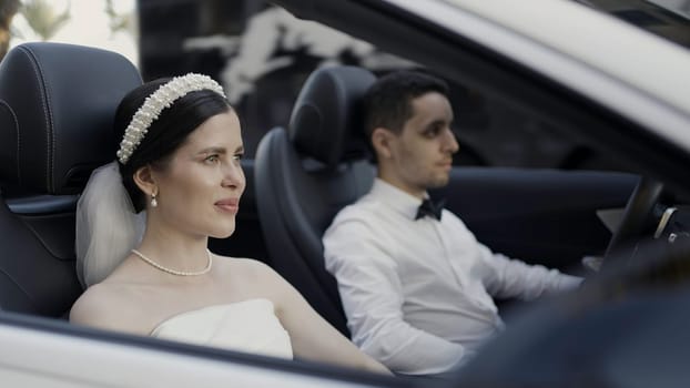 Bride and groom in wedding clothes sitting in cabriolet car. Action. Man and woman in luxury car