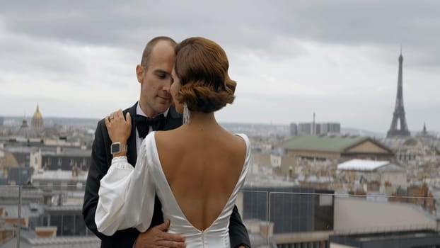 Couple enjoying each other on the background of Paris cityscape. Action. Elegant man in suit and woman in dress embracing in front of the Effel tower