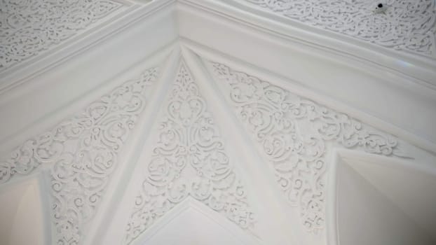 Low angle view of mosque interior. Scene. Ceiling inside majestic temple, carved ornament on white walls and ceiling