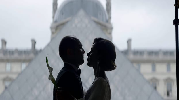 Happy couple near the Louvre museum pyramid in Paris. Action. Side view of embracing bride and groom