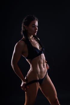 Slim tanned woman's body on dark grey background, studio shot