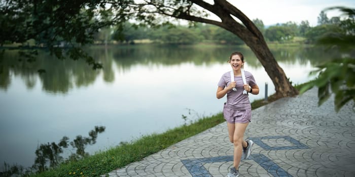 Jogging woman running in park on beautiful day off. Sport fitness model of asian ethnicity training outdoor for marathon.