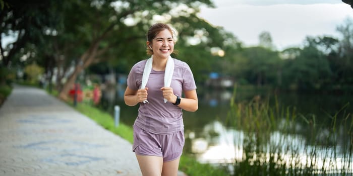 Jogging woman running in park on beautiful day off. Sport fitness model of asian ethnicity training outdoor for marathon.