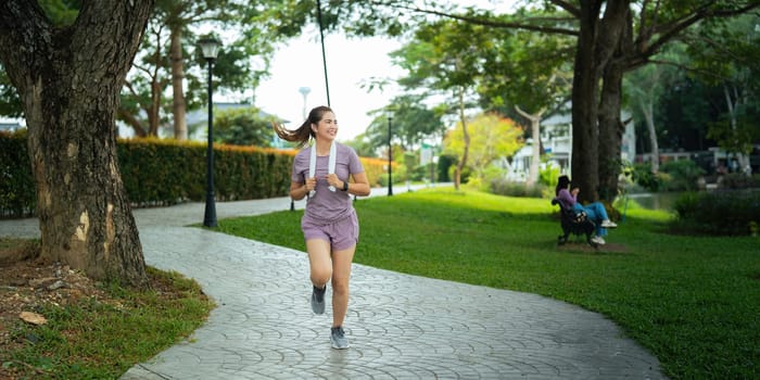 Jogging woman running in park on beautiful day off. Sport fitness model of asian ethnicity training outdoor for marathon.