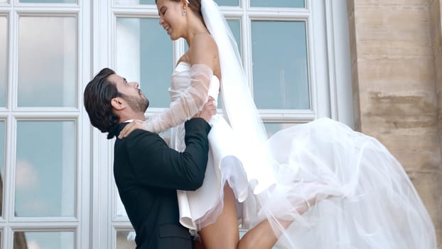 Beautiful couple of newlyweds at photo shoot on sunny day. Action. Attractive couple of newlyweds posing on background of old architecture. Couple of newlyweds with sunny summer day.