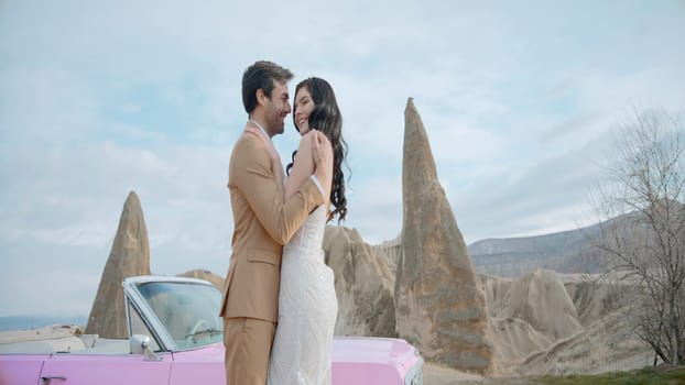 Beautiful wedding photo shoot in nature. Action.A bright tall couple who are in the mountains and stand next to a small pink Mercedes and pose hugging each other. High quality 4k footage